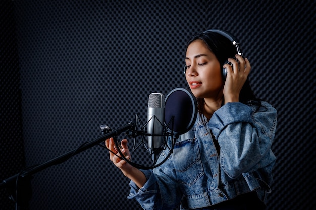 Joyeux joyeux assez souriant du portrait d'une jeune femme asiatique regarde le chanteur du smartphone portant des écouteurs enregistrant une chanson devant le microphone dans un studio professionnel