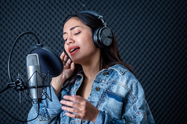 Joyeux joyeux joli sourire du portrait d'une jeune chanteuse asiatique portant des écouteurs enregistrant une chanson devant un microphone dans un studio professionnel