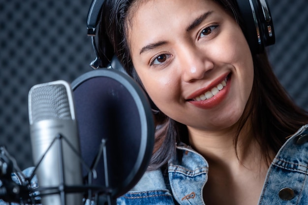 Joyeux joyeux joli sourire du portrait d'une jeune chanteuse asiatique portant des écouteurs enregistrant une chanson devant un microphone dans un studio professionnel