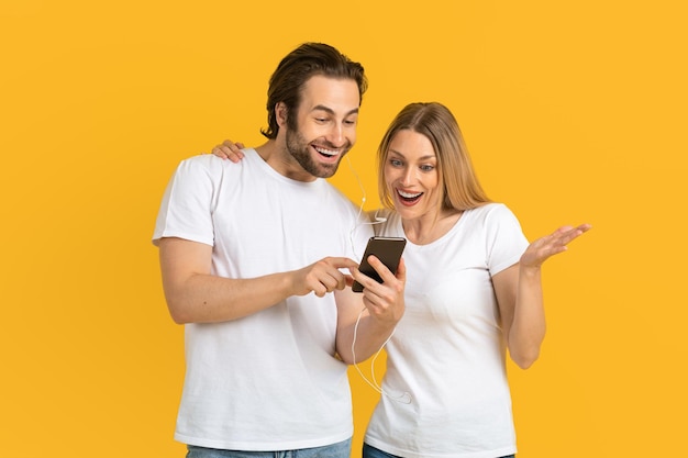 Joyeux mari européen du millénaire en t-shirt blanc montre le téléphone à sa femme surprise