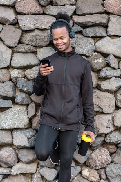 Joyeux mec afro-américain avec smartphone et tasse près du mur de pierre