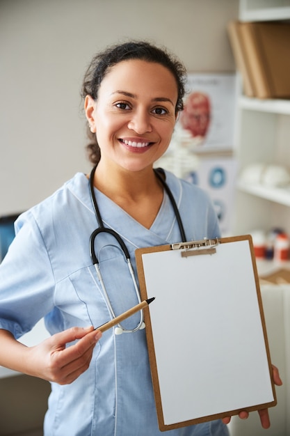 Joyeux médecin pointant son éco-stylo sur une feuille de papier blanc tout en se tenant à son bureau