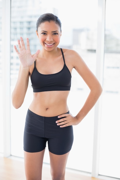 Joyeux modèle aux cheveux sombres en sportswear posant et saluant la caméra