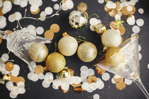 Joyeux Noël et Bonne Année Boules de Noël élégantes dans des verres de champagne et des confettis dorés sur la vue de dessus de fond festif Concept créatif de fête du nouvel an Bannière de vacances Moody