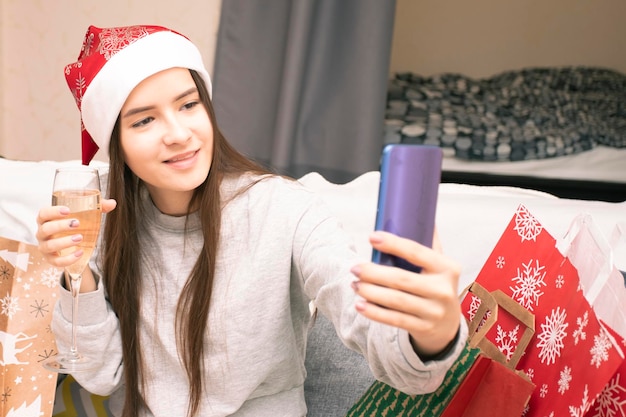 Joyeux Noël et bonne année jeune femme en bonnet de Noel félicite ses amis et sa famille en ligne avec une coupe de champagne