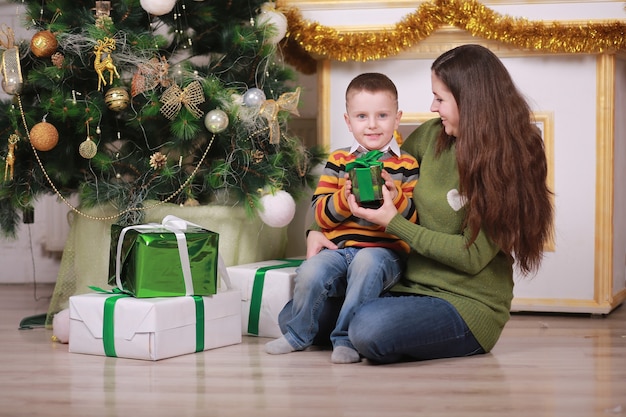 Joyeux Noël et bonnes fêtes. Jolie jeune maman avec son petit-fils amusant près de l'arbre de Noël avec des coffrets cadeaux à l'intérieur.