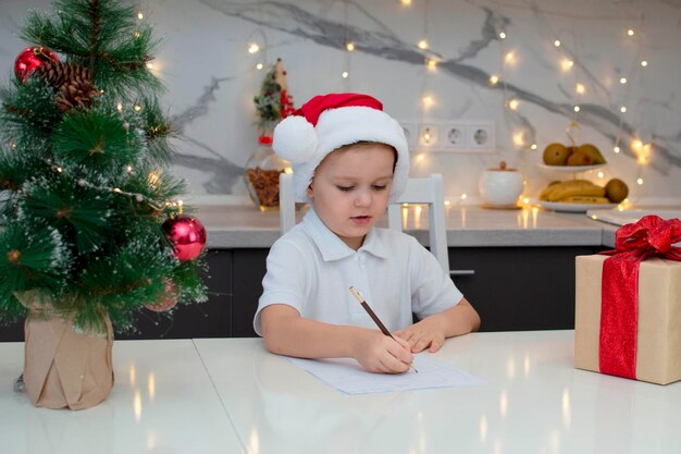 Joyeux Noël et bonnes vacances. Un garçon écrit une liste de souhaits au Père Noël à la maison à la table. Vacances, enfance, hiver, le concept de célébration. Mise au point sélective.