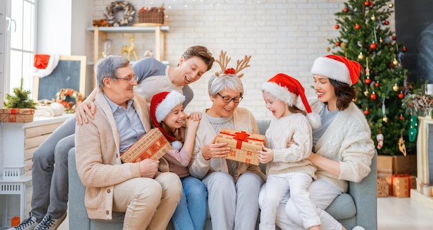 Joyeux Noël et bonnes vacances ! Grand-mère, grand-père, maman, papa et enfants échangeant des cadeaux. Parents et filles s'amusant près d'un arbre à l'intérieur. Famille aimante avec des cadeaux dans la chambre.