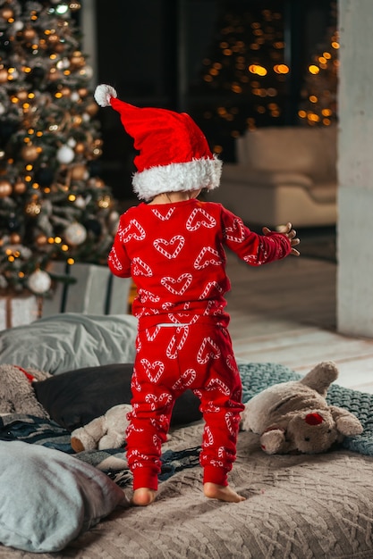 Joyeux Noël et bonnes vacances. Une petite fille en pyjama rouge et en chapeau de père noël