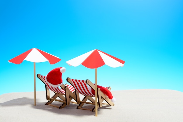 Joyeux Noël sur le concept de plage. Deux chaises longues avec parasols et chapeaux du Père Noël