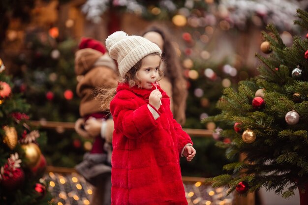 Joyeux Noël joyeuse petite fille dans un manteau de fourrure rouge à la foire en hiver