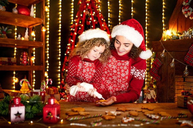 Joyeux Noël et joyeuses fêtes. Enthousiaste mignonne petite fille frisée et sa sœur aînée à chapeaux de pères Noël cuisiner des biscuits de Noël