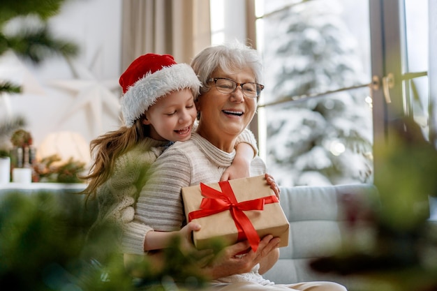 Photo joyeux noël et joyeuses fêtes une grand-mère joyeuse et sa mignonne petite-fille échangeant des cadeaux