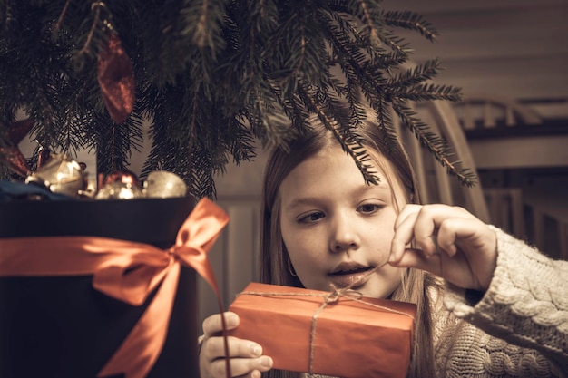 Joyeux Noël joyeuses fêtes Joyeuse petite fille blonde mignonne ouvre un cadeau de Noël