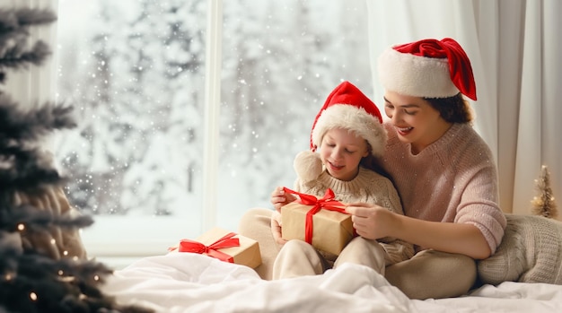 Photo joyeux noël et joyeuses fêtes maman joyeuse et sa jolie fille échangeant des cadeaux