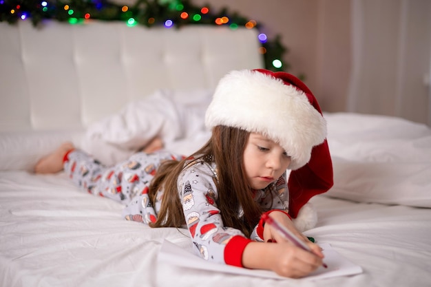 Joyeux Noël et joyeuses fêtes La petite fille heureuse sur le lit a écrit une lettre au Père Noël