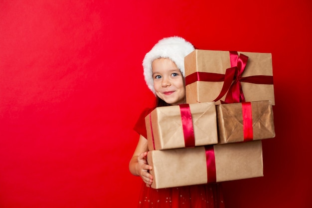 Joyeux Noël et joyeuses fêtes Portrait d'une fille émotive dans une casquette de Père Noël sur fond rouge