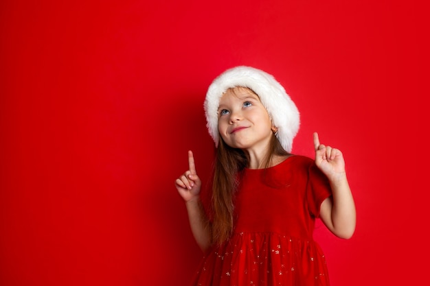 Joyeux Noël et joyeuses fêtes Portrait d'une fille émotive dans une casquette de Père Noël sur fond rouge