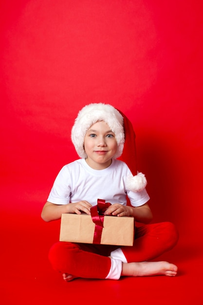 Joyeux Noël. Portrait d'un garçon mignon dans une casquette de père Noël avec des coffrets cadeaux sur fond rouge. Un endroit pour le texte. photo de haute qualité