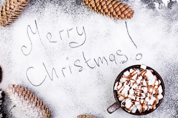 Joyeux Noël texte à la main sur la neige. Guimauve sucrée de Noël avec du chocolat dans une tasse brune