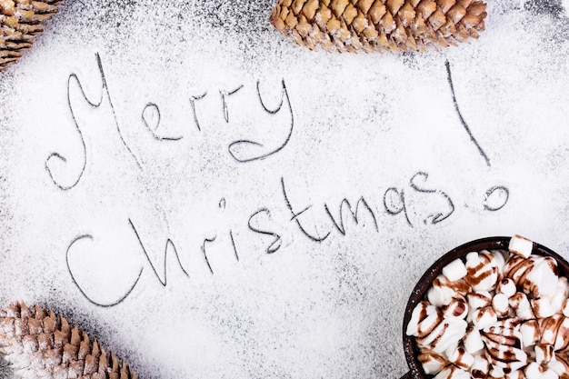 Joyeux Noël texte à la main sur la neige. Guimauve sucrée de Noël avec du chocolat dans une tasse brune