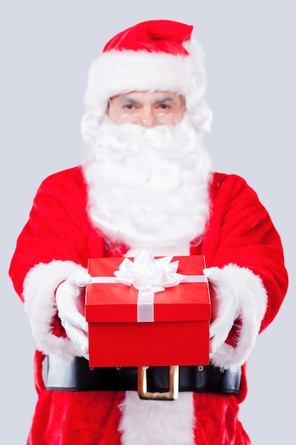 Joyeux Noël à toi ! Le Père Noël traditionnel s'étendant sur une boîte-cadeau en se tenant debout sur un fond gris