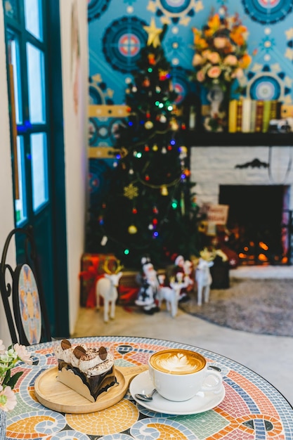 Photo joyeux noëlhot coffee latte avec de la mousse de lait latte art dans une tasse et un gâteau au chocolat fait maison avec des décors de noël et des boules d'arbre de noël sur un bureau en marbre célébrant joyeux noël et nouvel an