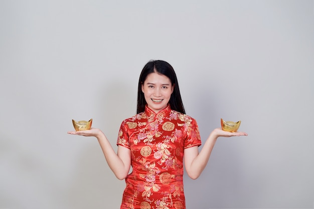 Joyeux Nouvel An chinois. Portrait belle jeune femme asiatique porter une robe chinoise tenant des lingots d'or isolés sur fond gris studio