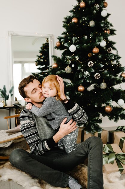 Joyeux papa embrassant une jolie petite fille près de l'arbre de Noël Joyeux Noël et joyeuses fêtes Père et petit enfant s'amusant et jouant ensemble à la maison Gros plan