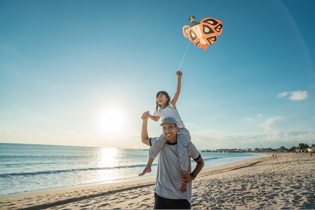 Joyeux papa et fille faisant voler un cerf-volant ensemble à la plage