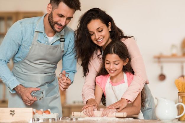 Joyeux parents et fille préparant une pâtisserie et étalant la pâte pour les biscuits cuisinant et passant du temps