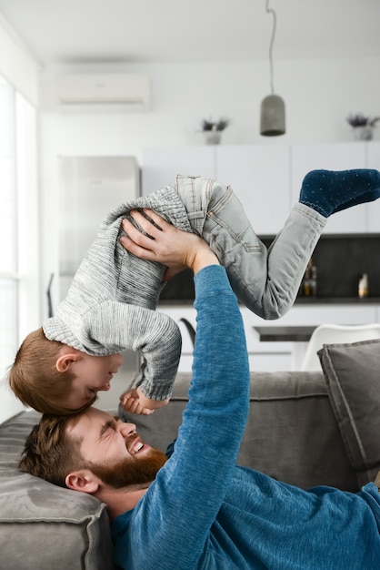 joyeux père barbu vêtu d'une chemise bleue jouant avec son petit fils mignon dans la chambre