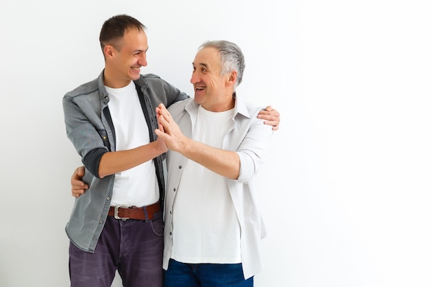 Joyeux père et fils étreignant et posant ensemble isolés sur mur blanc