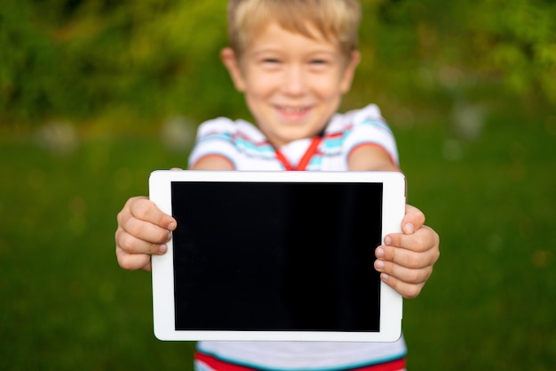 Joyeux petit bébé tient une tablette à l'extérieur dans un parc d'été, gros plan sur les mains des enfants