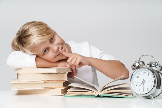 Joyeux Petit écolier Faisant Ses Devoirs Au Bureau, Lisant Des Livres Isolés Sur Un Mur Gris