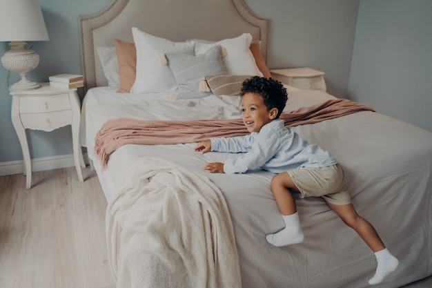 Joyeux petit enfant afro-américain profitant de la récréation à l'intérieur sur le lit