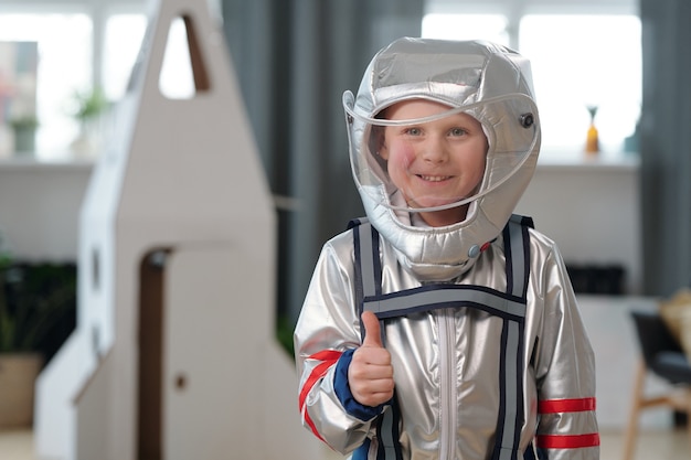 Joyeux petit garçon en combinaison spatiale montrant le pouce vers le haut