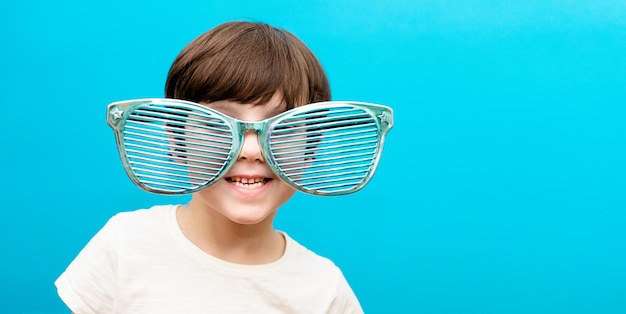 Photo joyeux petit garçon dans de grands verres sourit sur fond bleu