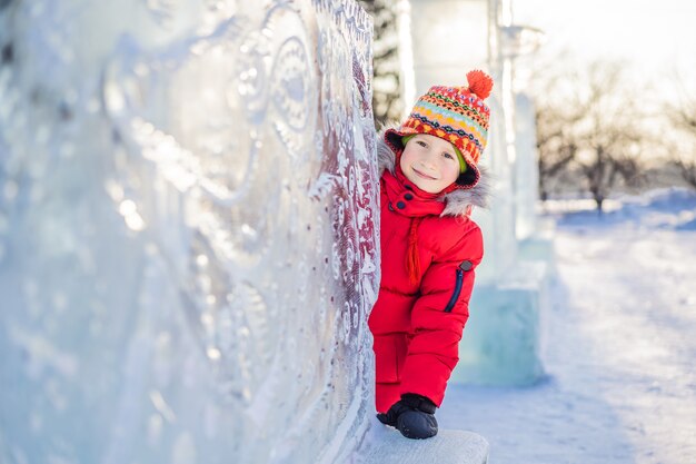 Joyeux petit garçon sur le fond de la sculpture de glace. Plaisirs d'hiver amusants dans la neige