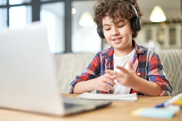 Joyeux petit garçon latino-américain portant des écouteurs regardant l'écran d'un ordinateur portable tout en