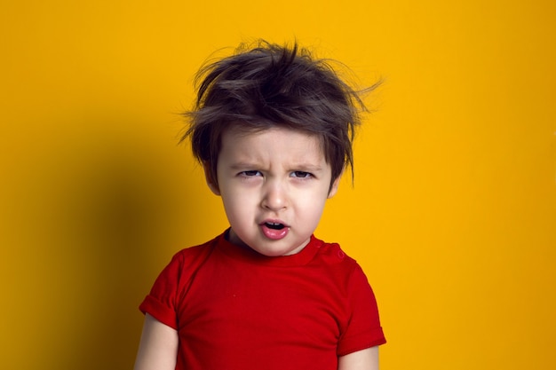 Joyeux petit garçon en t-shirt rouge se dresse sur fond jaune