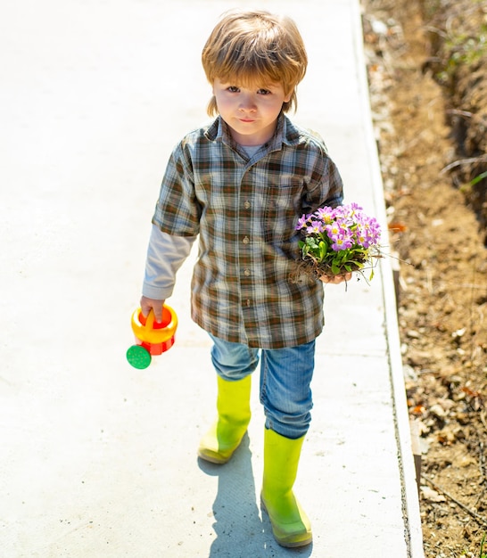 Joyeux petit jardinier aux fleurs printanières. Enfant agriculteur travaillant dans le champ. J'aime passer du temps à la ferme. Petite aide dans le jardin.