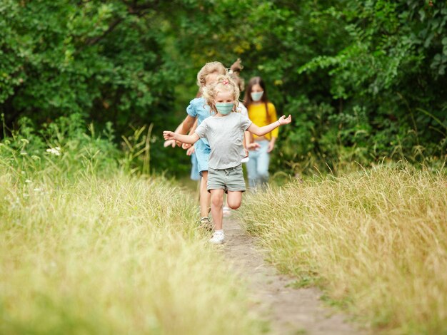 Joyeux petits enfants portant un masque protecteur sautant et courant sur un pré, une forêt. Semble heureux, joyeux, sincère. Espace de copie. Enfance, concept de pandémie. Santé, pandémie de coronavirus.