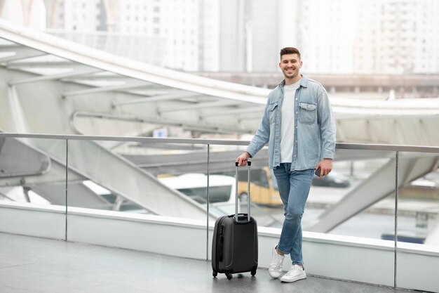 Joyeux touriste debout avec une valise de voyage posant à l'aéroport