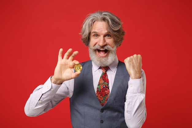 Joyeux Vieil Homme Barbu Moustache Aux Cheveux Gris En Chemise Classique Gilet Cravate Isolé Sur Fond Rouge. Concept De Style De Vie Des Gens. Maquette De L'espace De Copie. Tenez Le Bitcoin, Future Monnaie, Faites Le Geste Du Gagnant.