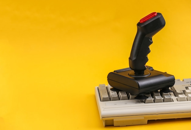 Joystick rétro sur l'ancien clavier du PC. Fond jaune. Attributs années 80, jeu