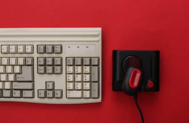 Joystick rétro et vieux clavier pc sur fond rouge. Jeux, compétition de jeux vidéo. Vue de dessus