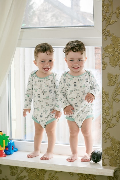 Jumeaux joyeux - les frères se tiennent sur le rebord de la fenêtre