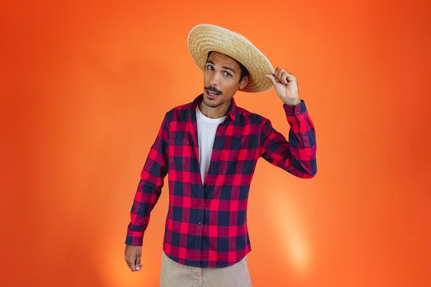 Junina Party Black Man With Outfit Holding Hat Isolé sur fond orange Jeune homme portant des vêtements traditionnels pour Festa Junina Festival brésilien de juin