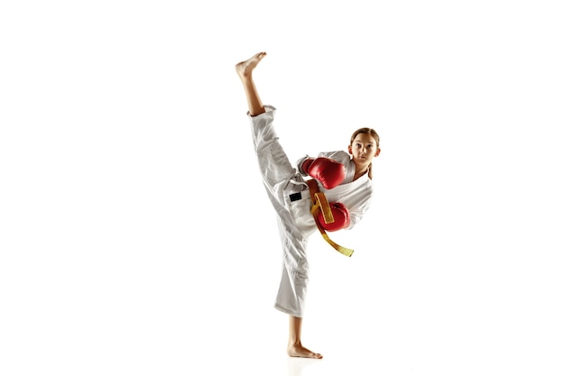 Junior confiant en kimono pratiquant le combat au corps à corps, les arts martiaux. Jeune combattante avec entraînement de ceinture jaune sur mur blanc. Concept de mode de vie sain, sport, action.